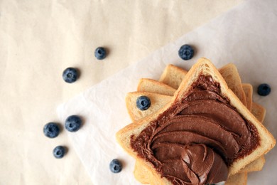 Photo of Tasty toast with chocolate paste and blueberries on parchment paper, flat lay