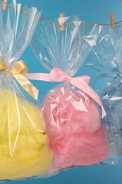 Packaged sweet cotton candies hanging on clothesline against light blue background, closeup