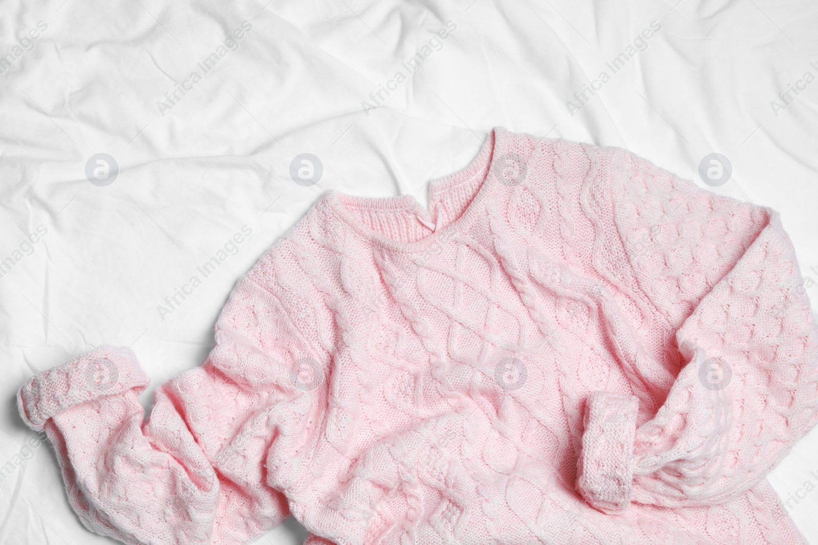 Photo of Pink knitted sweater on white fabric, flat lay