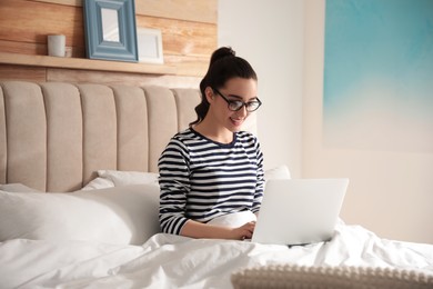 Photo of Young woman working with laptop on bed at home