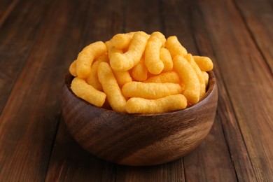 Bowl of tasty cheesy corn puffs on wooden table