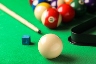 Photo of Many colorful billiard balls, cue and chalk on green table, closeup