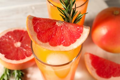 Photo of Tasty grapefruit drink with ice in glass, rosemary and fresh fruits on light table, closeup