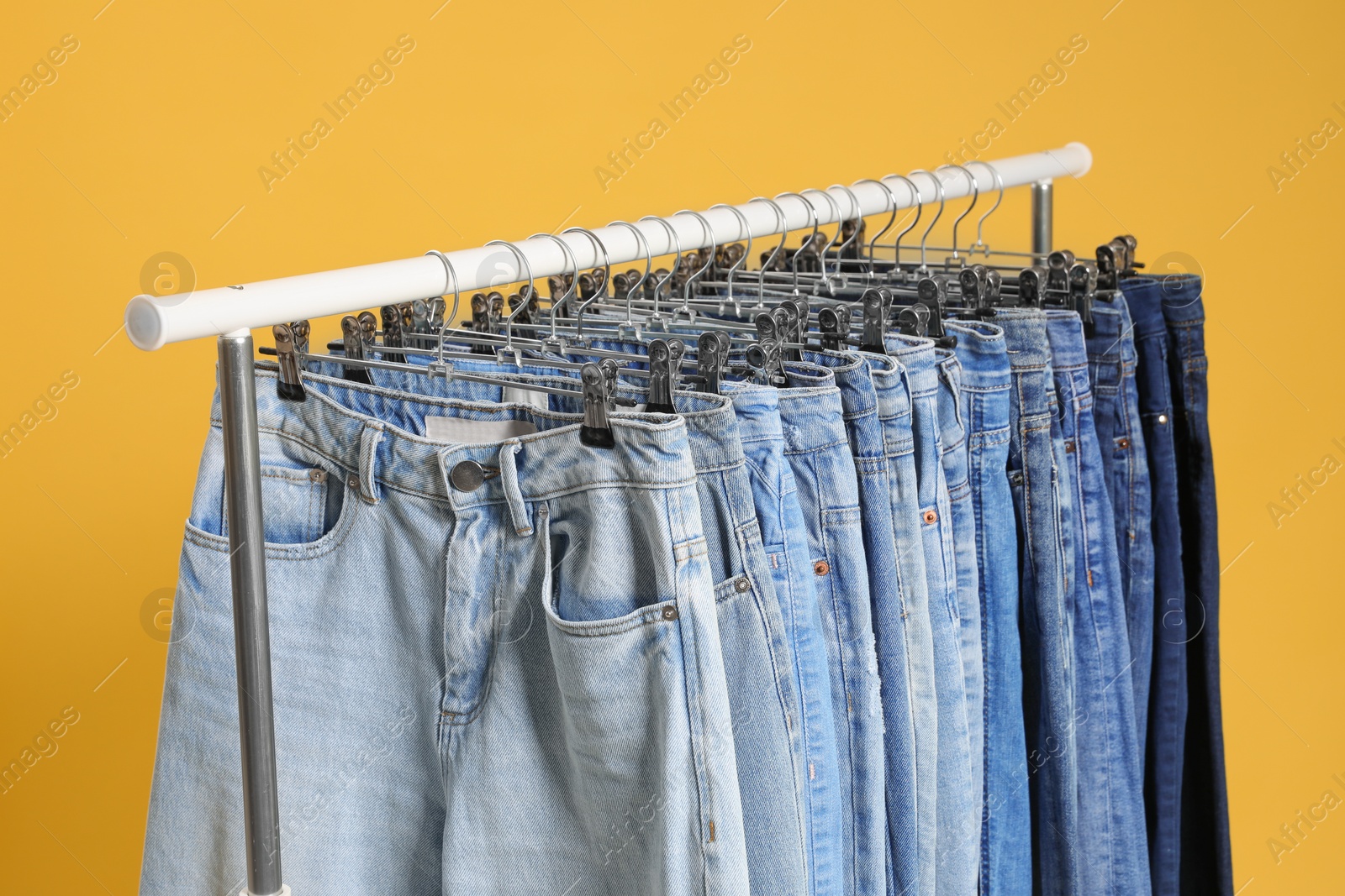 Photo of Rack with different jeans on yellow background