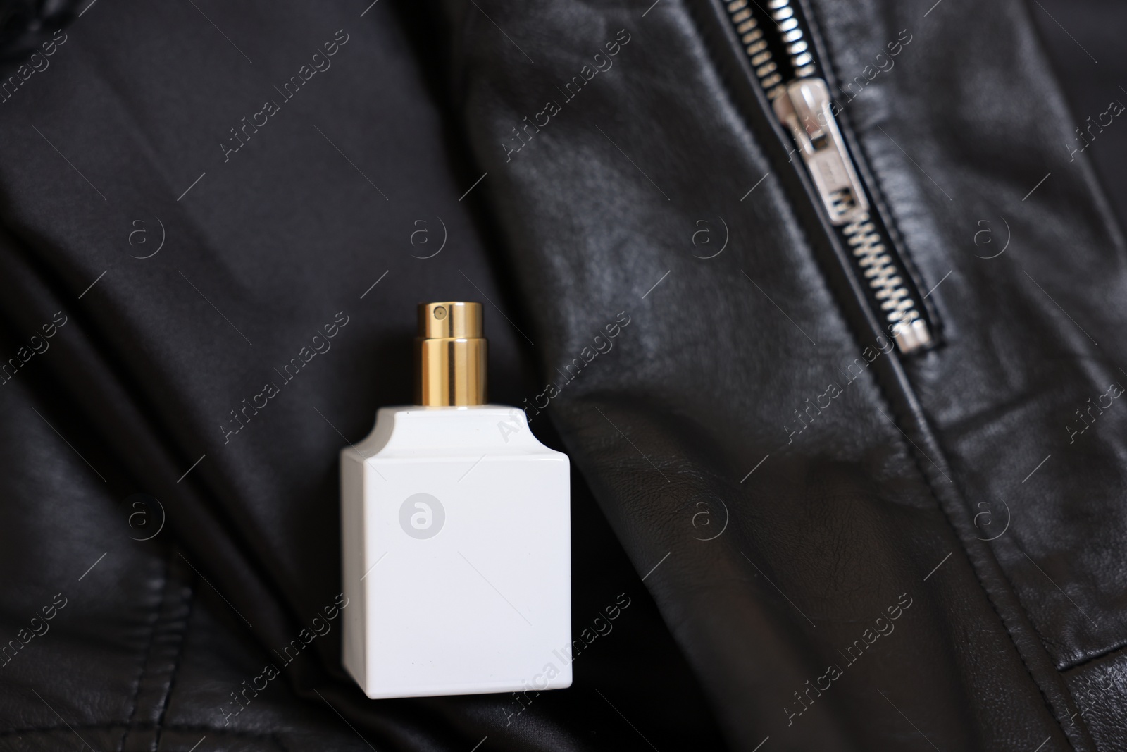 Photo of Bottle of fragrant perfume on black leather jacket, top view