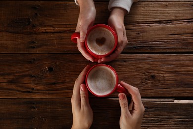 Photo of Women with mugs of hot coffee at wooden table, top view