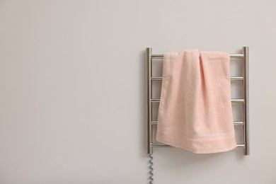 Photo of Heated rail with pink towel on white wall, space for text