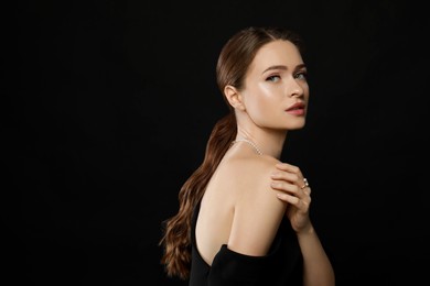 Photo of Young woman wearing elegant pearl jewelry on black background, space for text