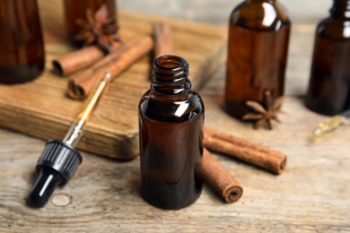 Photo of Bottles of essential oils and cinnamon sticks on wooden table