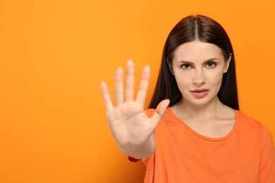 Photo of Woman showing stop gesture on orange background. Space for text
