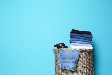 Stack of different jeans on basket against color wall with space for text