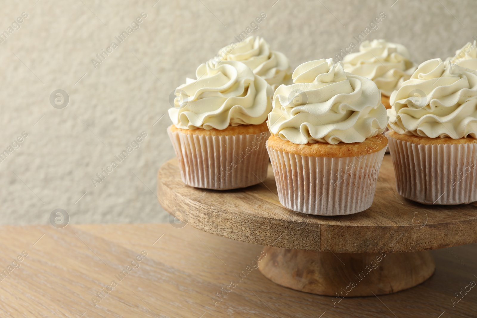 Photo of Tasty vanilla cupcakes with cream on wooden table, space for text