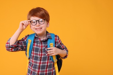Photo of Happy schoolboy in glasses on orange background. Space for text