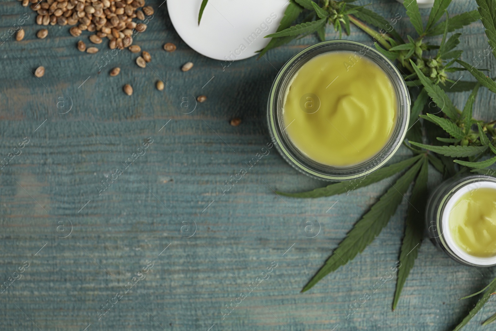 Photo of Jars of hemp cream and seeds on blue wooden table, flat lay with space for text. Organic cosmetics
