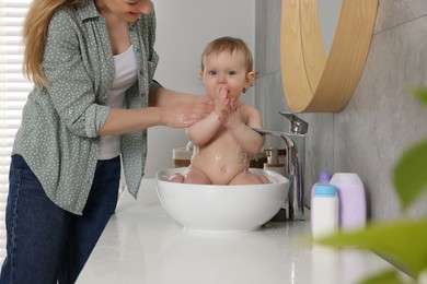 Mother washing her little baby in sink at home