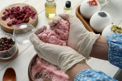 Photo of Woman in gloves holding bath bomb mixture at white table, closeup