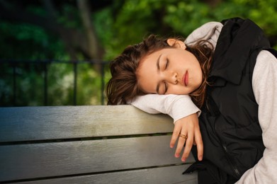 Photo of Tired woman sleeping on wooden bench outdoors