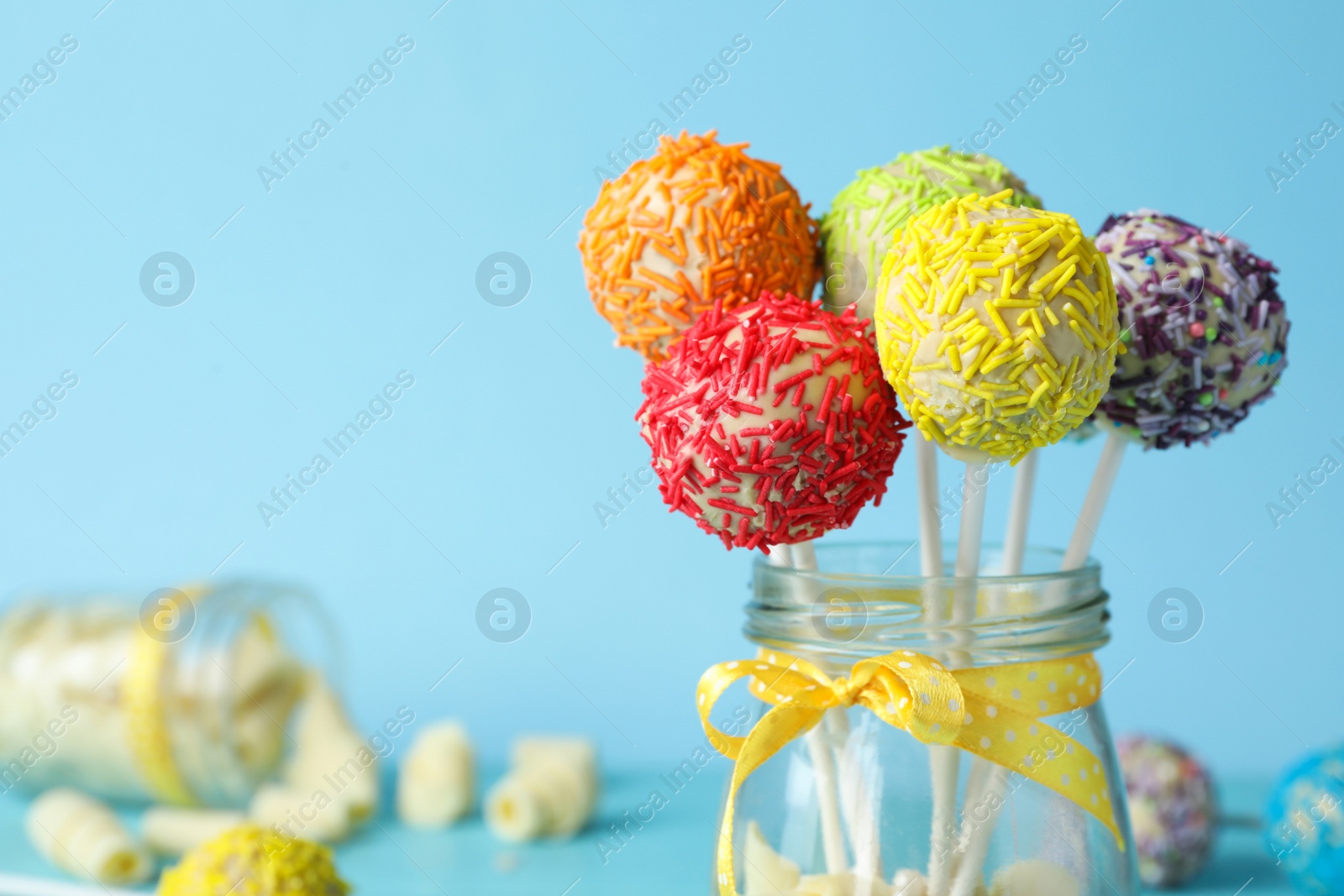 Photo of Yummy bright cake pops in glass jar with bow on color background. Space for text