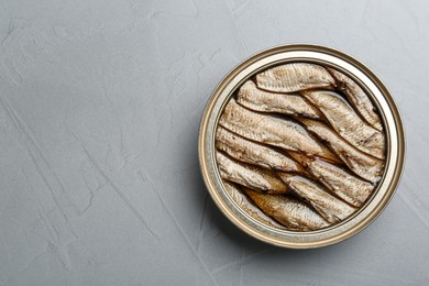 Photo of Open tin can of sprats on light grey table, top view. Space for text