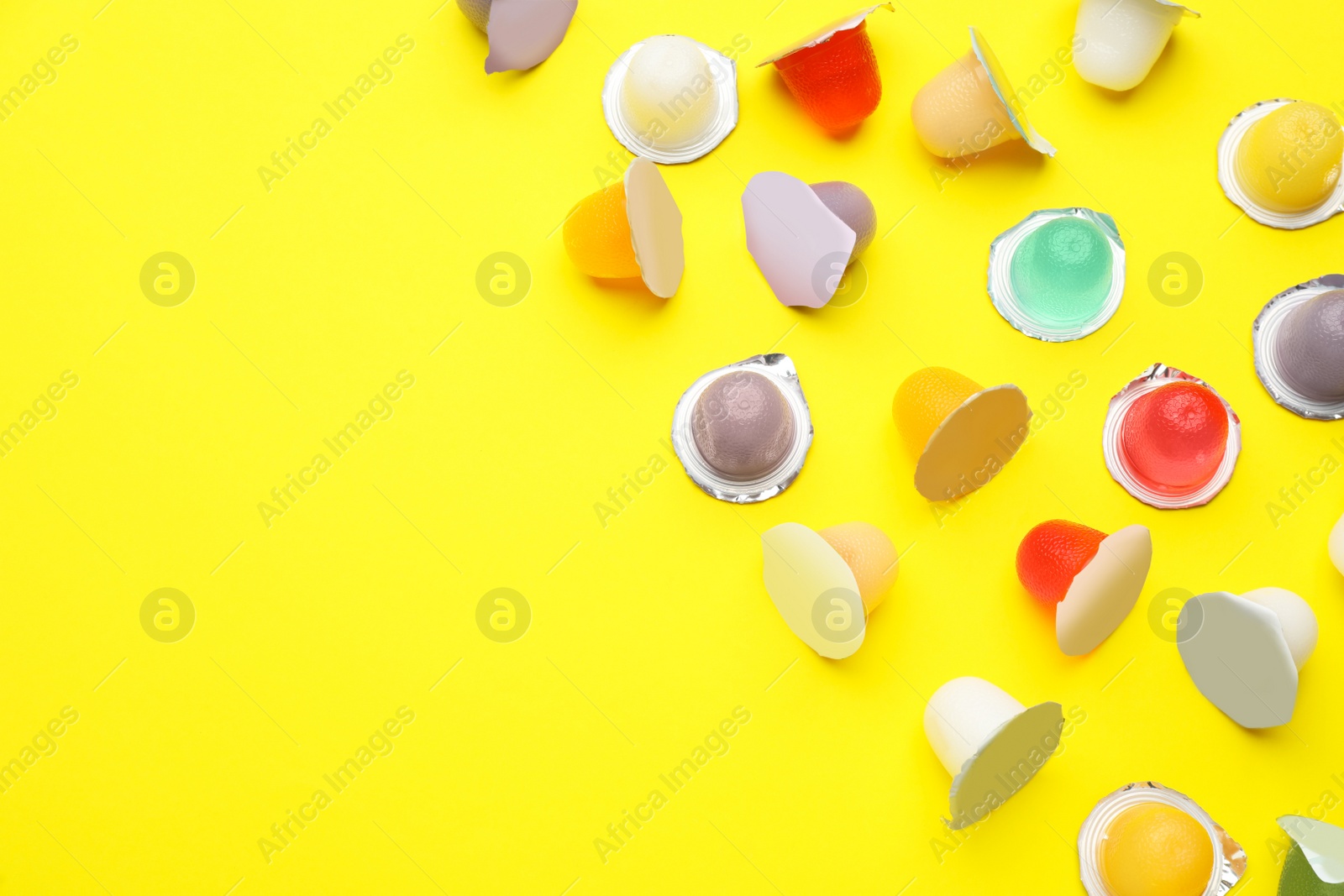 Photo of Tasty bright jelly cups  on yellow background, flat lay. Space for text