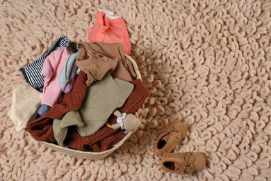 Photo of Laundry basket with baby clothes, shoes and crochet toy on beige rug, flat lay