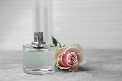 Photo of Bottle of perfume and rose on grey table indoors, space for text