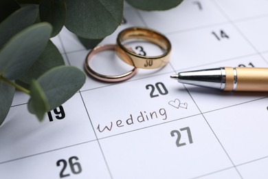 Photo of Calendar with date reminder about Wedding Day, pen and rings, closeup