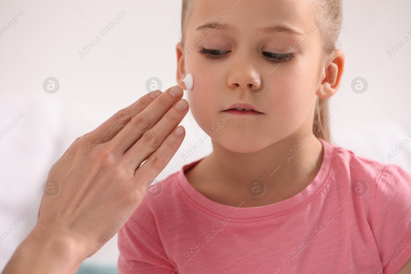 Photo of Mother applying ointment onto her daughter's cheek on white background, closeup