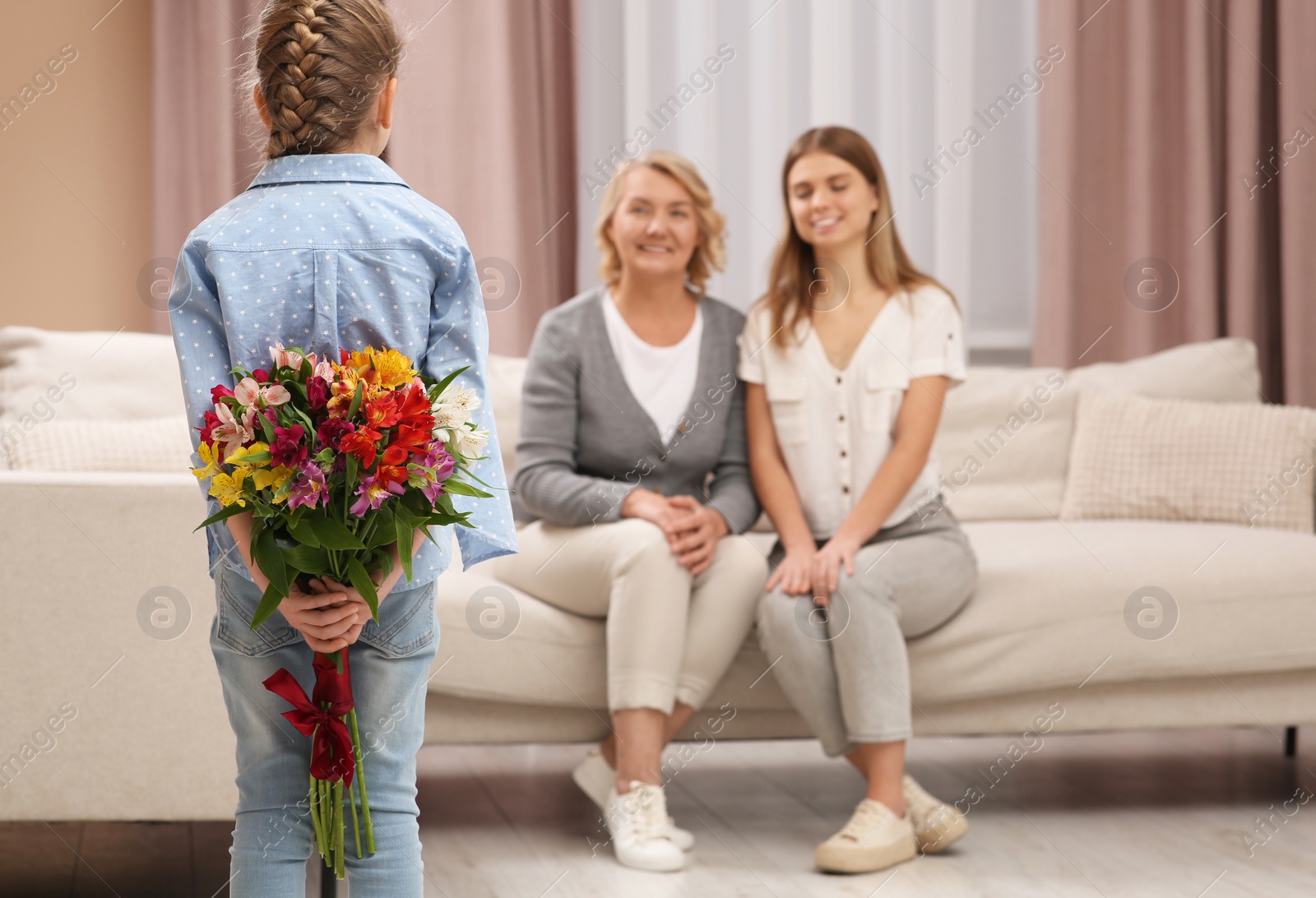 Photo of Little girl congratulating her mom and granny with flowers at home. Happy Mother's Day