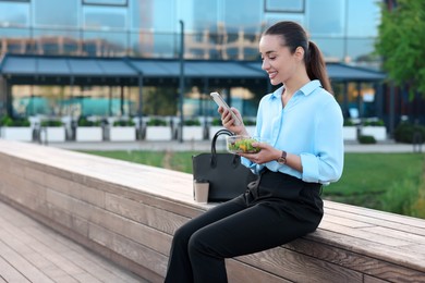 Smiling businesswoman using smartphone during lunch outdoors. Space for text