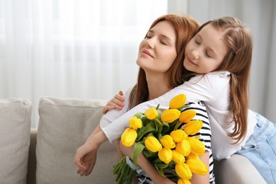 Photo of Mother and her cute daughter with bouquet of yellow tulips at home. Space for text
