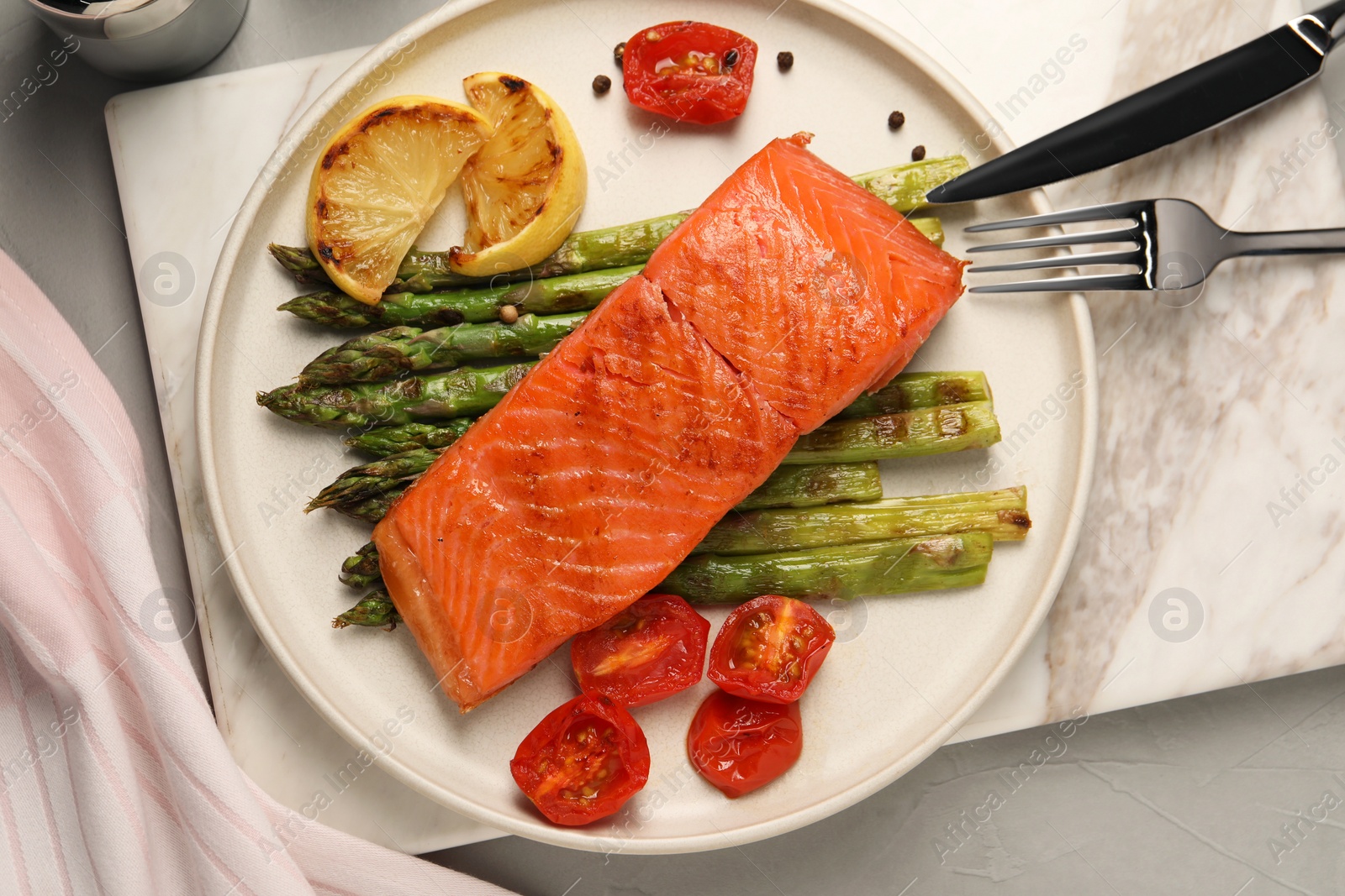 Photo of Tasty grilled salmon with asparagus, tomatoes, spices and lemon served on light grey table, top view