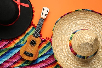 Mexican sombrero hats, guitar and colorful poncho on orange background, flat lay