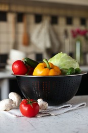 Photo of Metal colander with different wet vegetables on white textured table, closeup