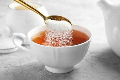 Adding sugar into cup of tea at grey textured table, closeup