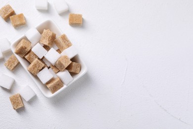 Photo of Different sugar cubes in bowl on white table, top view. Space for text