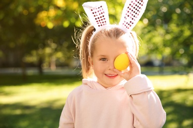 Photo of Cute little girl with bunny ears holding Easter egg in park