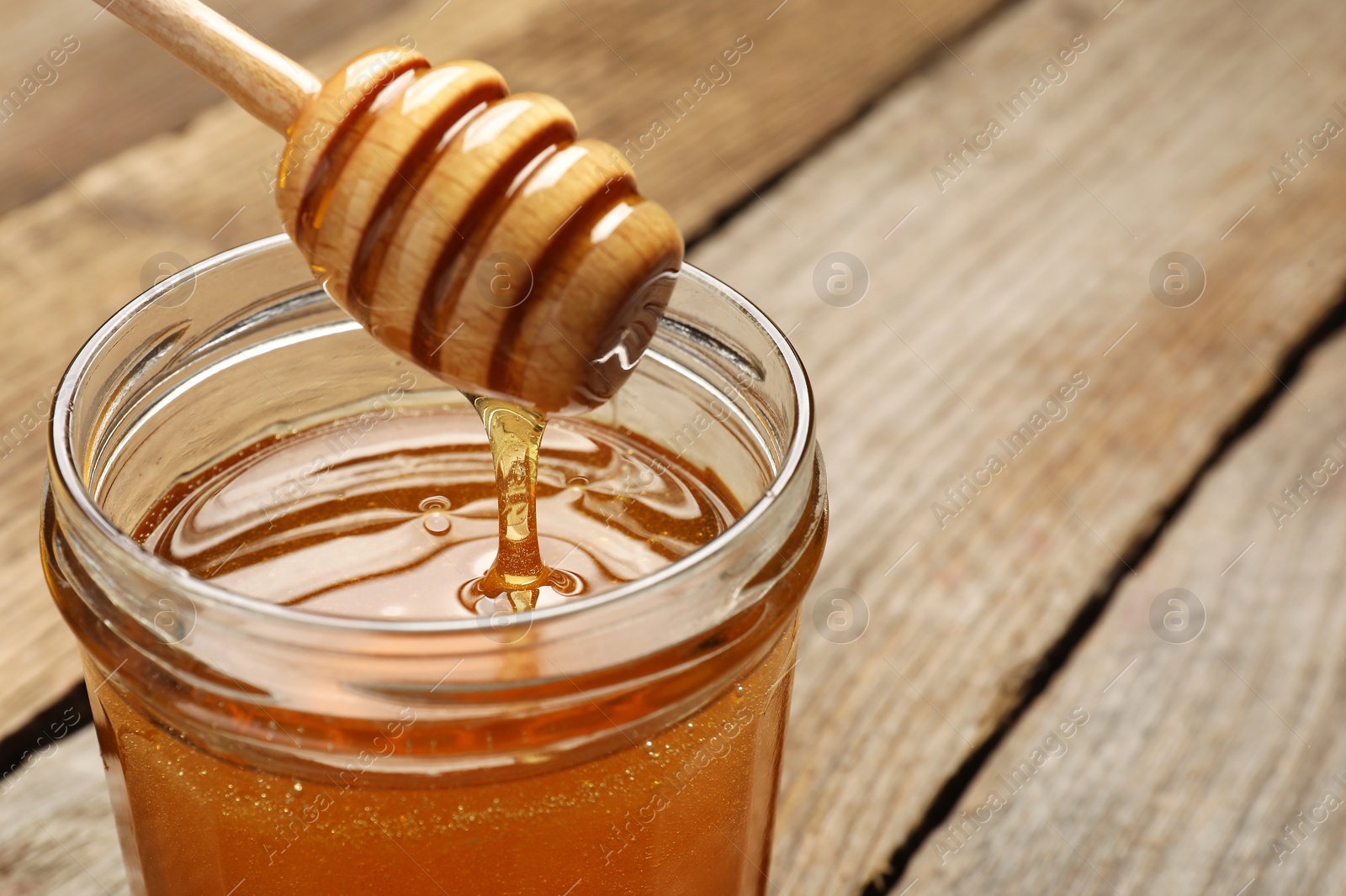 Photo of Pouring honey from dipper into jar on table, closeup. Space for text