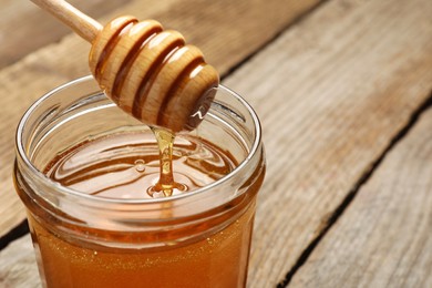 Photo of Pouring honey from dipper into jar on table, closeup. Space for text