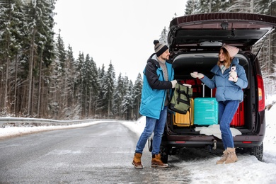 Photo of Couple near open car trunk full of luggage on road, space for text. Winter vacation
