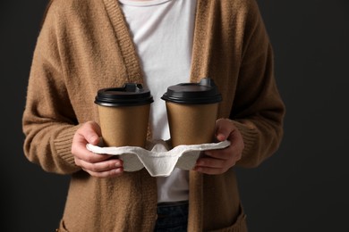 Photo of Woman holding takeaway cardboard cups on black background, closeup. Coffee to go