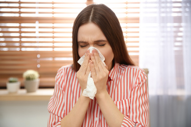 Photo of Sick young woman sneezing at workplace. Influenza virus