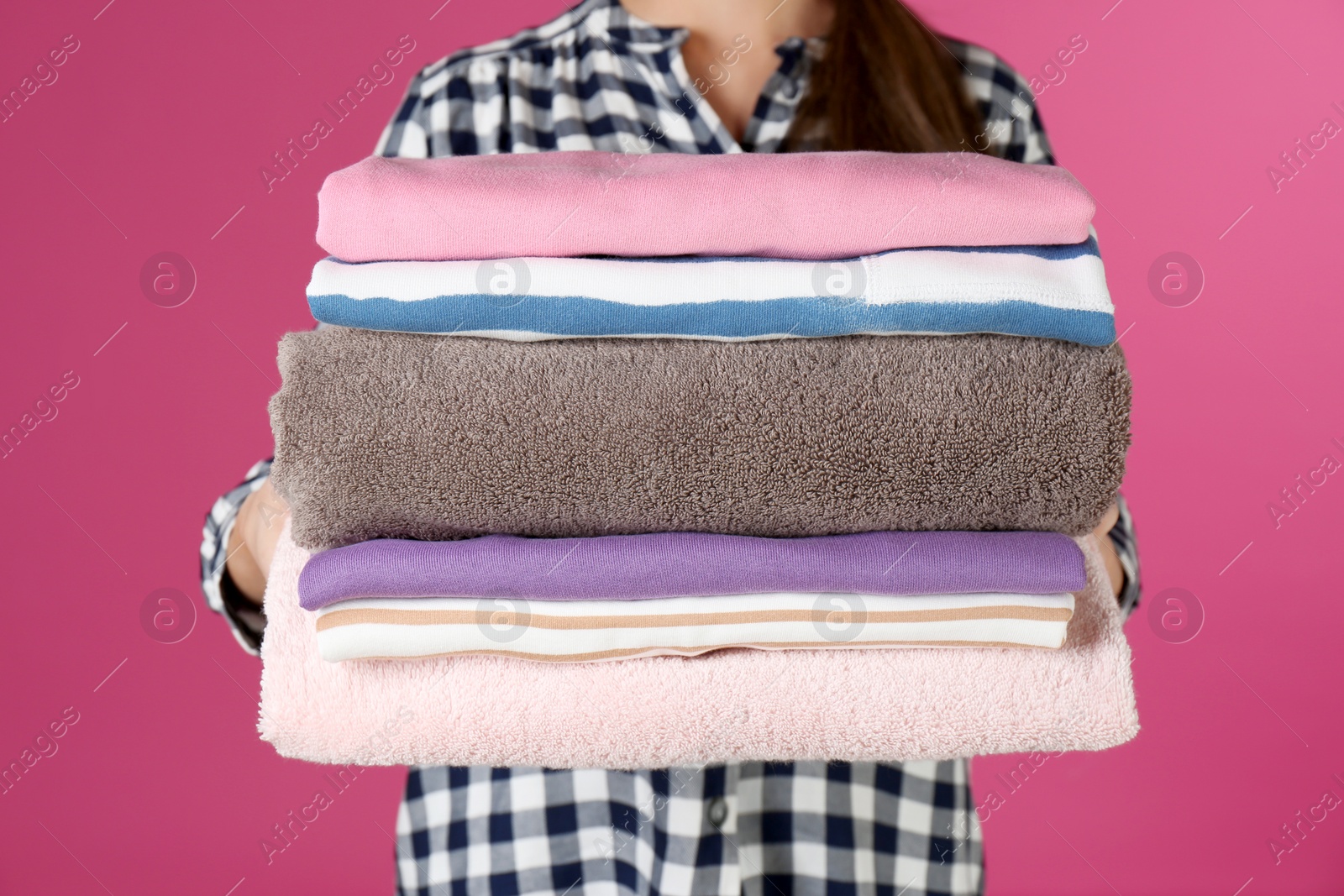 Photo of Young woman holding clean laundry on color background, closeup