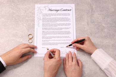 Man and woman signing marriage contract at light grey table, top view