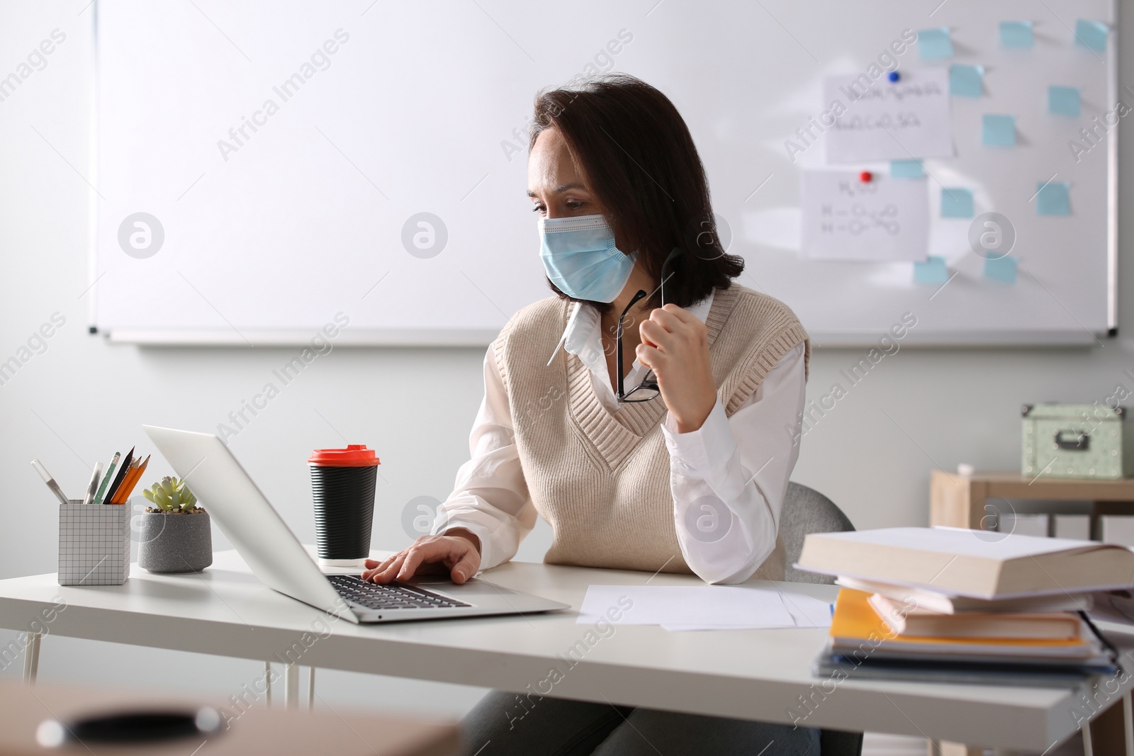Photo of Teacher with protective mask conducting online lesson in classroom during COVID-19 quarantine