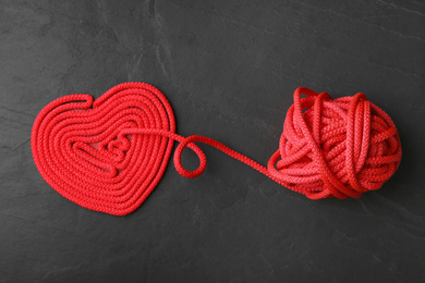 Heart made of yarn on black stone background, flat lay. Relationship problems concept