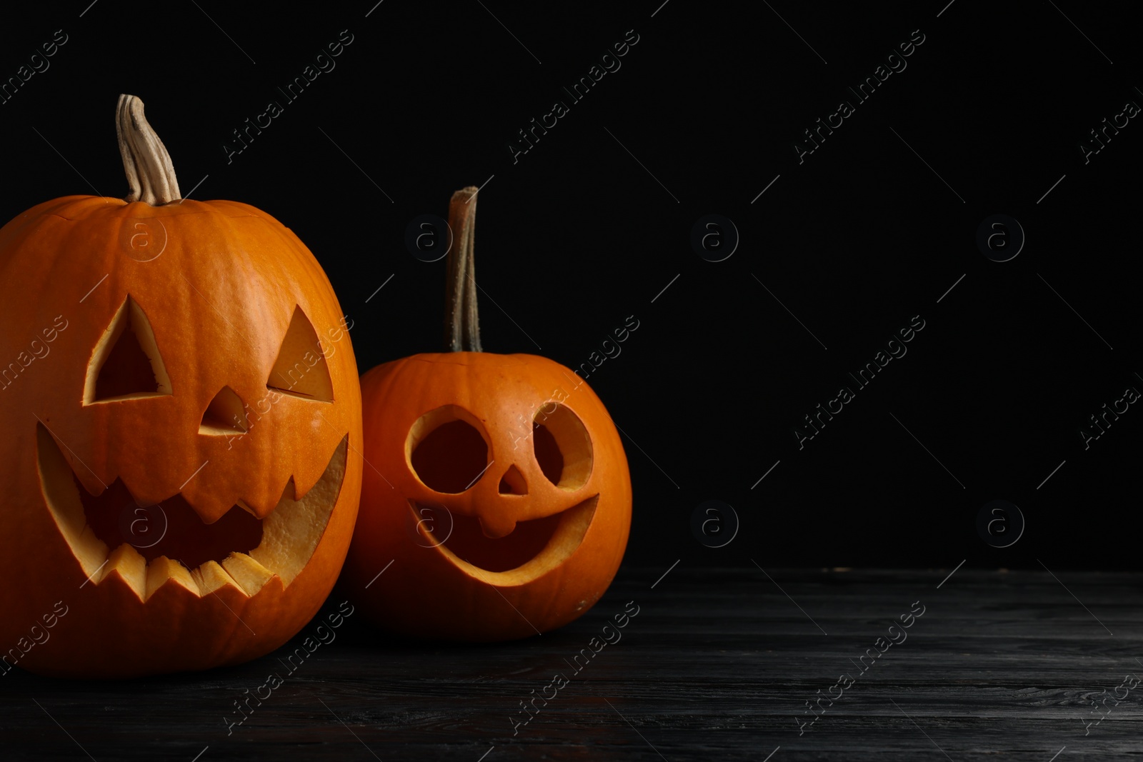 Photo of Scary jack o'lanterns made of pumpkins on wooden table against black background, space for text. Halloween traditional decor