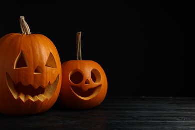 Photo of Scary jack o'lanterns made of pumpkins on wooden table against black background, space for text. Halloween traditional decor