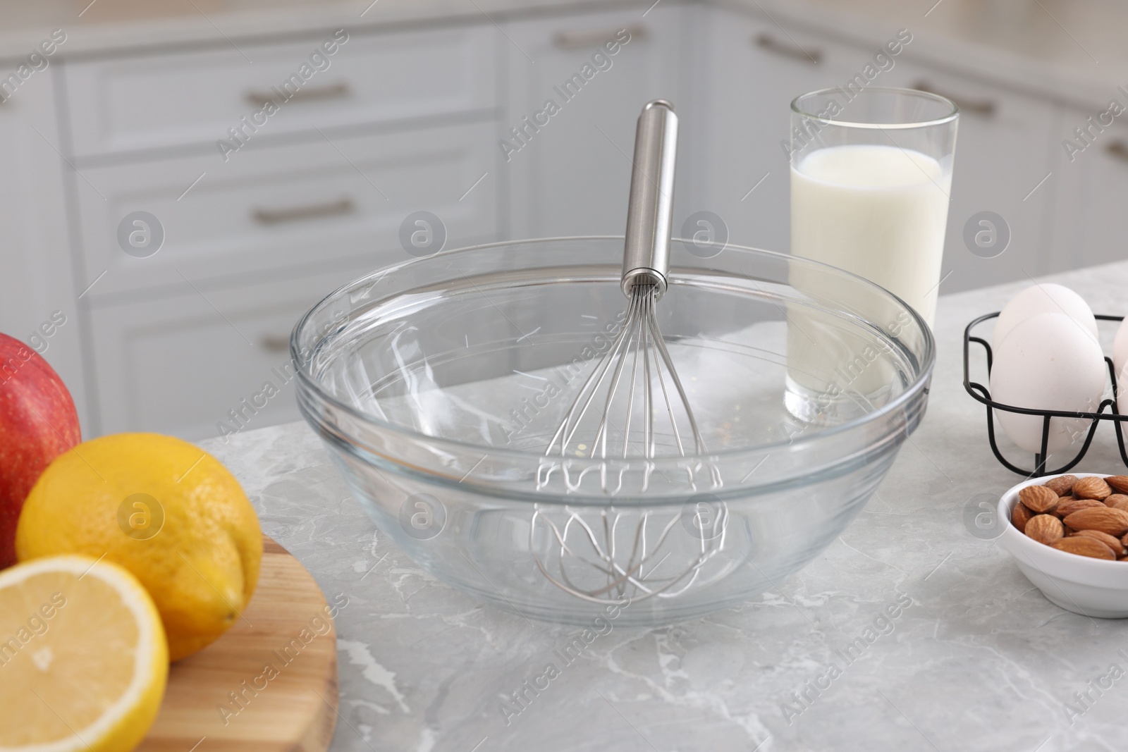 Photo of Metal whisk, bowl and different products on gray marble table in kitchen