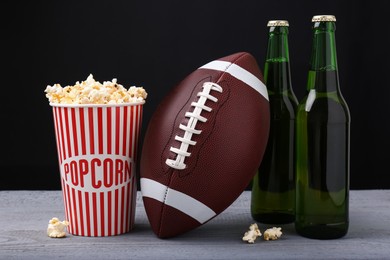 Photo of American football ball with popcorn and beer on grey wooden table